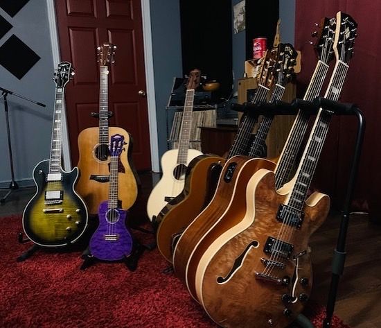 A row of electric and acoustic guitars and ukuleles on stands