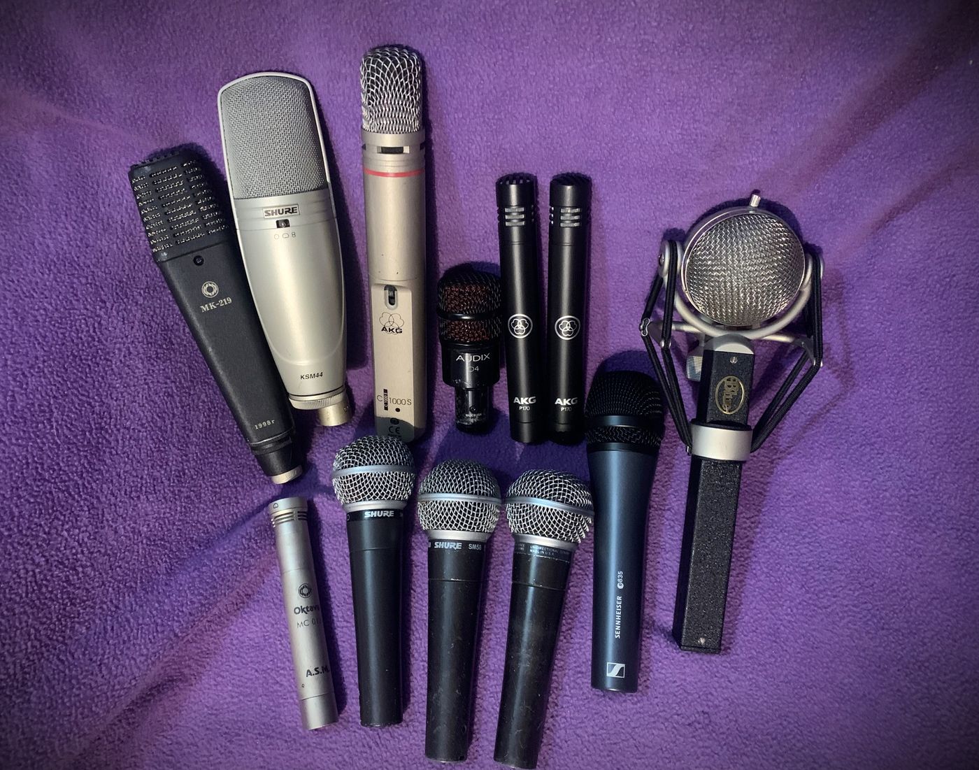 A collection of studio microphones laid out on purple fabric